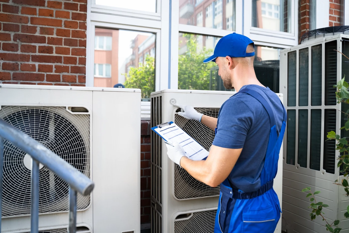 HVAC technician with a clipboard assessing outdoor air conditioning equipment