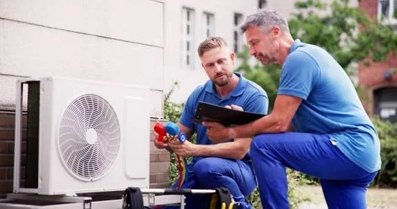 Two HVAC technicians checking an outdoor unit with gauges and a clipboard